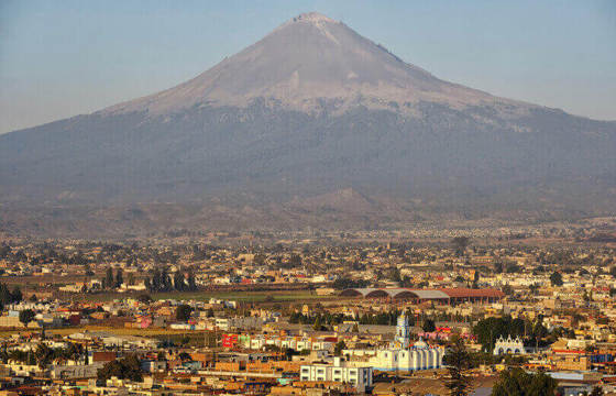Aerial view of Puebla with Popocatepetl volcano rising in the background under a clear blue sky. 