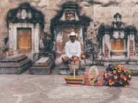 Mexican street vendor with colourful flowers and baskets sits by a rustic colonial wall, capturing local charm and heritage. 