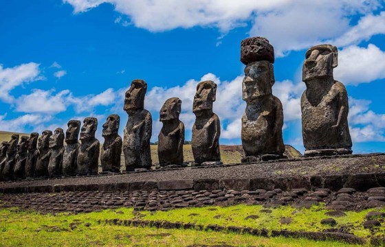 A row of towering Moai statues stands on a stone platform under a bright sky on Chile's Easter Island. 