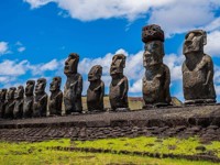 A row of towering Moai statues stands on a stone platform under a bright sky on Chile's Easter Island. 
