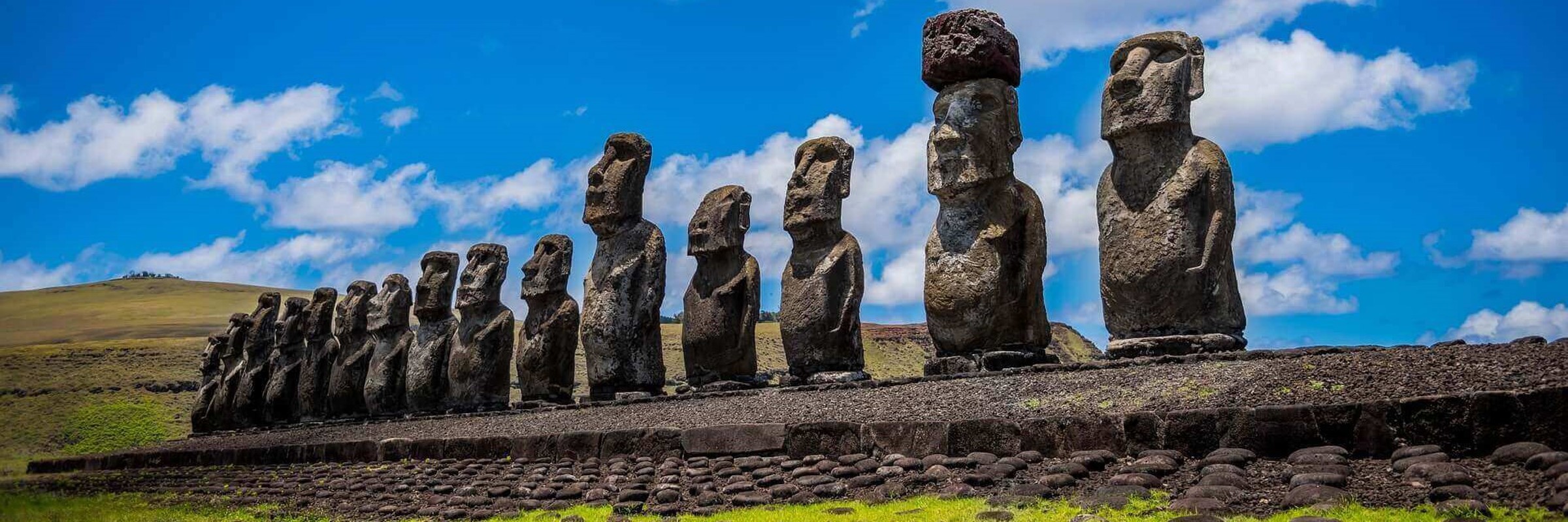 A row of towering Moai statues stands on a stone platform under a bright sky on Chile's Easter Island. 