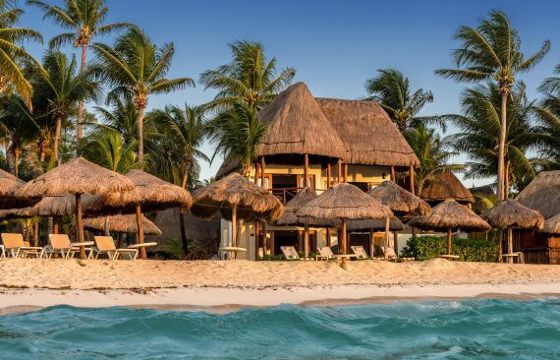 Beachfront view of Mahekal Beach Resort in Playa del Carmen, with palm trees, thatched-roof cabanas, and turquoise Caribbean waters. 