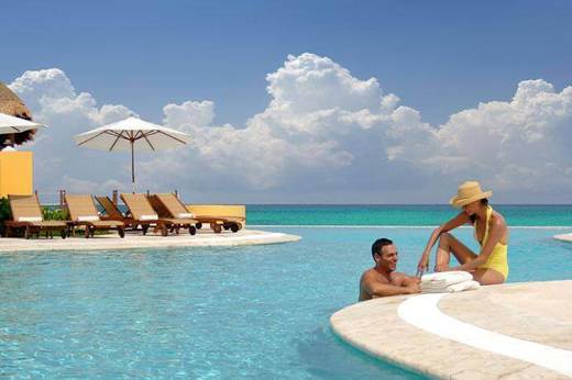 Relaxing at a luxury infinity pool at Fairmont Mayakoba, Mexico, with ocean views and tropical cabanas. 