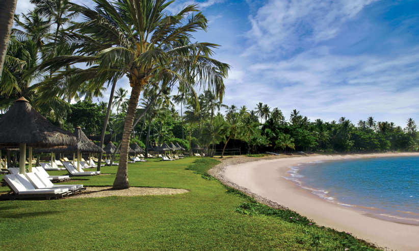 Beachfront view with palm trees, sun loungers, and blue skies at Tivoli Eco Resort in Bahia, Brazil. 