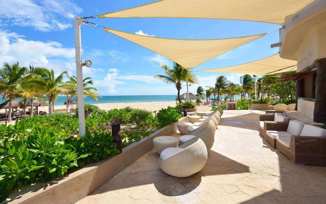 Beachfront outdoor lounge with modern seating and sunshades at Catalonia Playa Maroma Resort, Riviera Maya, Mexico. 