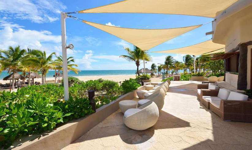 Beachfront outdoor lounge with modern seating and sunshades at Catalonia Playa Maroma Resort, Riviera Maya, Mexico. 