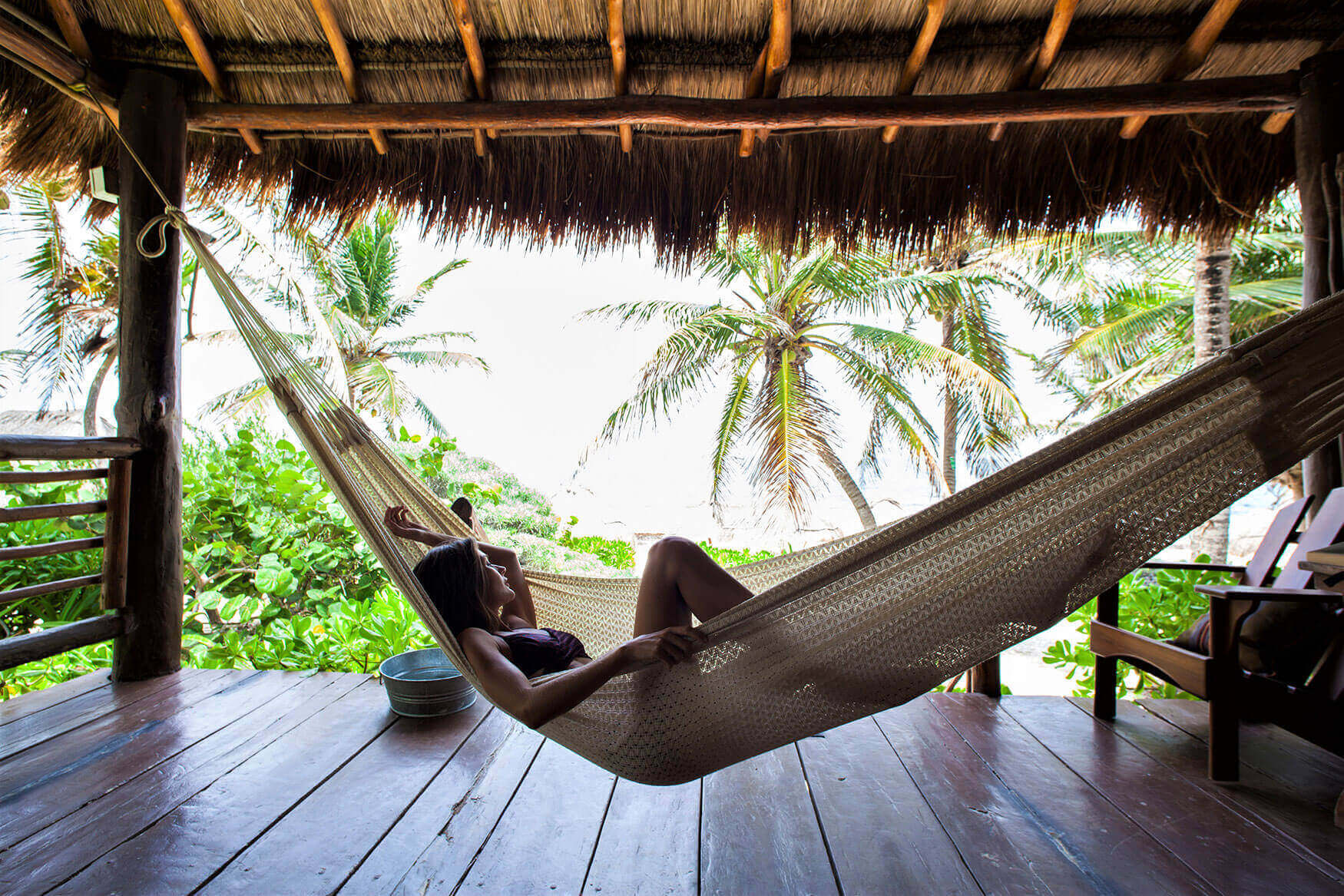 Guests relaxing in a hammock with an ocean breeze and palm tree views at a beachfront hotel in Tulum, Mexico. 