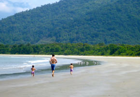 Father and children walking along the tranquil beach of Angra dos Reis, Brazil with lush forested hills in the background. 