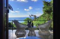 Private balcony with elegant white wicker chairs overlooking lush greenery and the Pacific Ocean. 