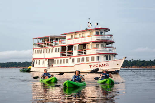 Guests kayaking on the Amazon River with the Tucano expedition cruise boat in the background. 