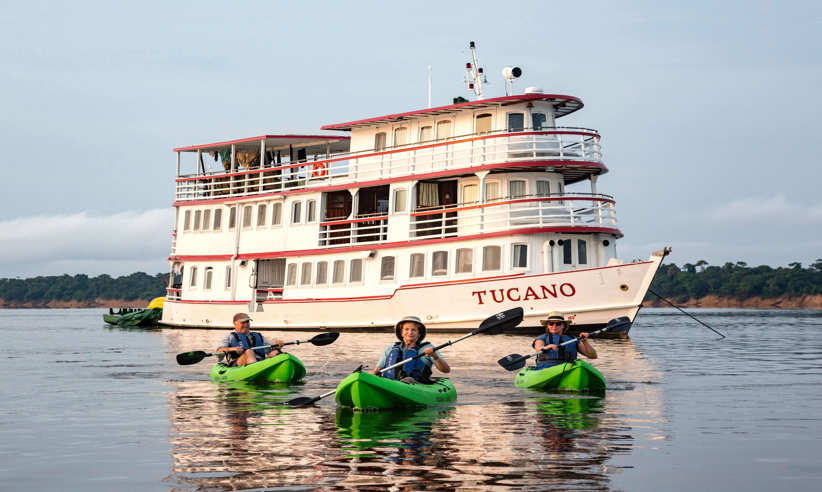 Guests kayaking on the Amazon River with the Tucano expedition cruise boat in the background. 