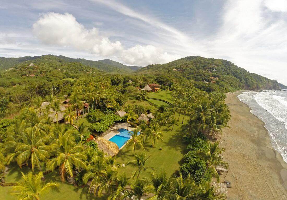 Aerial view of a secluded coastal lodge surrounded by dense tropical forest. 