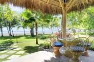 Thatched-roof beach hut with rustic wicker chairs and table, overlooking palm trees and the Pacific Ocean at Playa Esterillos. 
