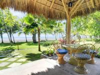 Thatched-roof beach hut with rustic wicker chairs and table, overlooking palm trees and the Pacific Ocean at Playa Esterillos. 