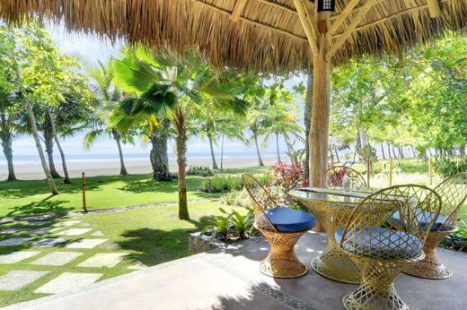 Thatched-roof beach hut with rustic wicker chairs and table, overlooking palm trees and the Pacific Ocean at Playa Esterillos. 