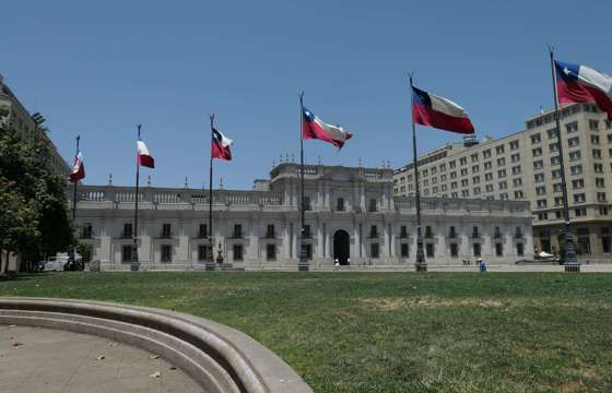 La Moneda Palace in Santiago, Chile framed by waving national flags on a clear day in the capital's civic center. 