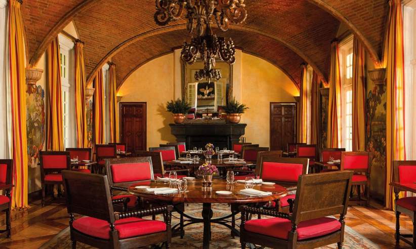 Elegant colonial-style hotel dining room with red chairs, arched ceiling, and warm ambient lighting in Mexico. 