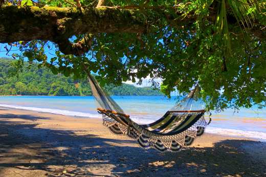A hammock sways in the shade, overlooking the tranquil beach and turquoise waters of Playa Cativo. 