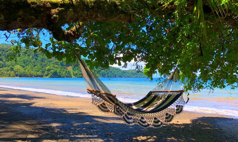 A hammock sways in the shade, overlooking the tranquil beach and turquoise waters of Playa Cativo. 