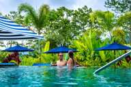 Couple enjoying a tropical escape in the infinity pool at Nayara Springs, surrounded by lush greenery and vibrant umbrellas. 