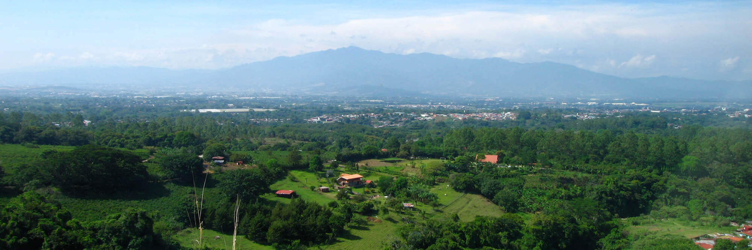 A panoramic view of San Jose and Alajuela with scattered homes and lush greenery set against misty central mountains.