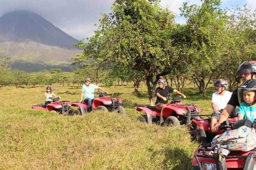Group on quad bikes exploring scenic countryside with Arenal Volcano in the background.