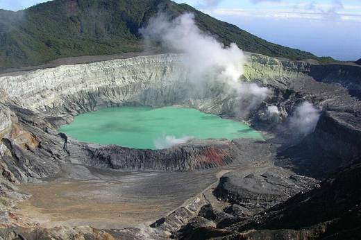 A dramatic view of Poas Volcano's smoking crater with vivid turquoise waters surrounded by steep rocky walls in Costa Rica. 