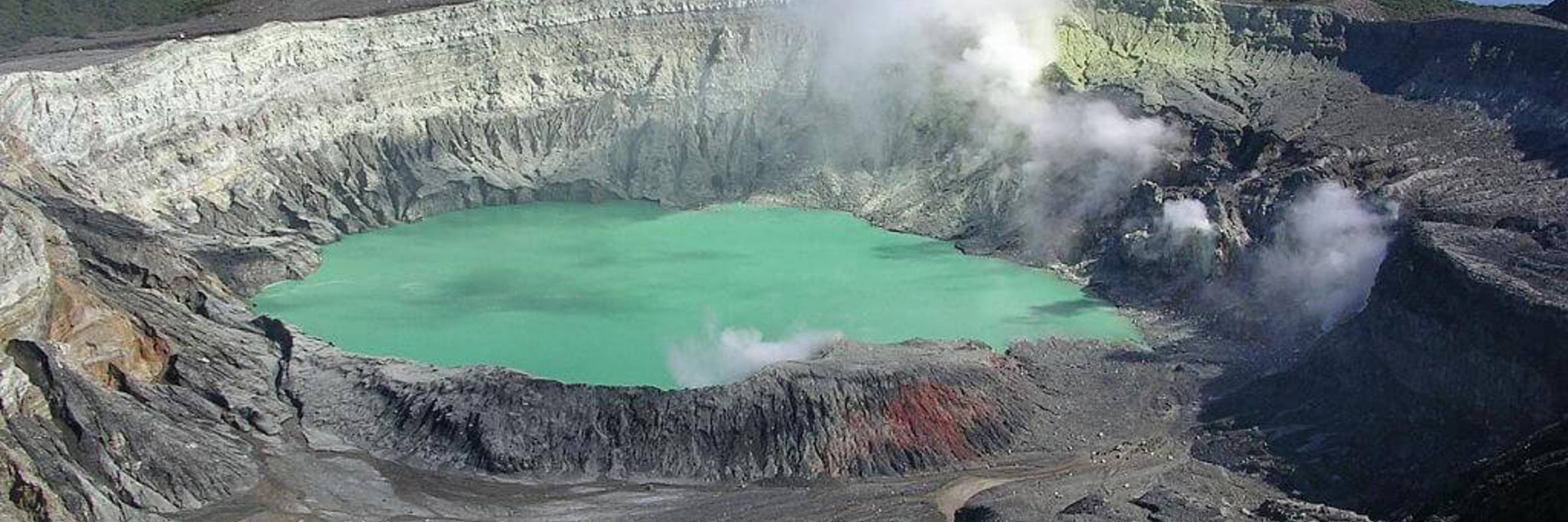 A dramatic view of Poas Volcano's smoking crater with vivid turquoise waters surrounded by steep rocky walls in Costa Rica. 