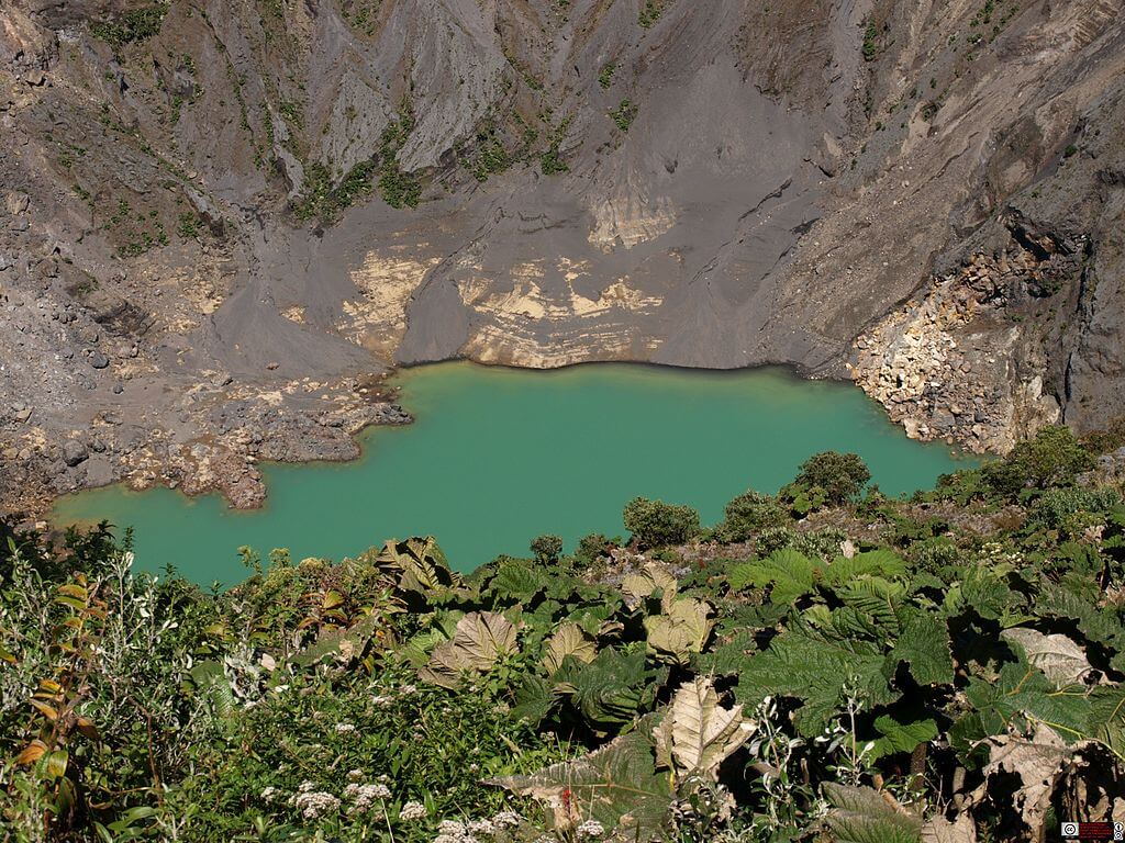 Emerald-green crater lake at Irazu Volcano, surrounded by rugged cliffs and alpine vegetation in Costa Rica. 