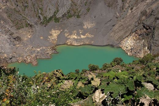 Emerald-green crater lake at Irazu Volcano, surrounded by rugged cliffs and alpine vegetation in Costa Rica. 