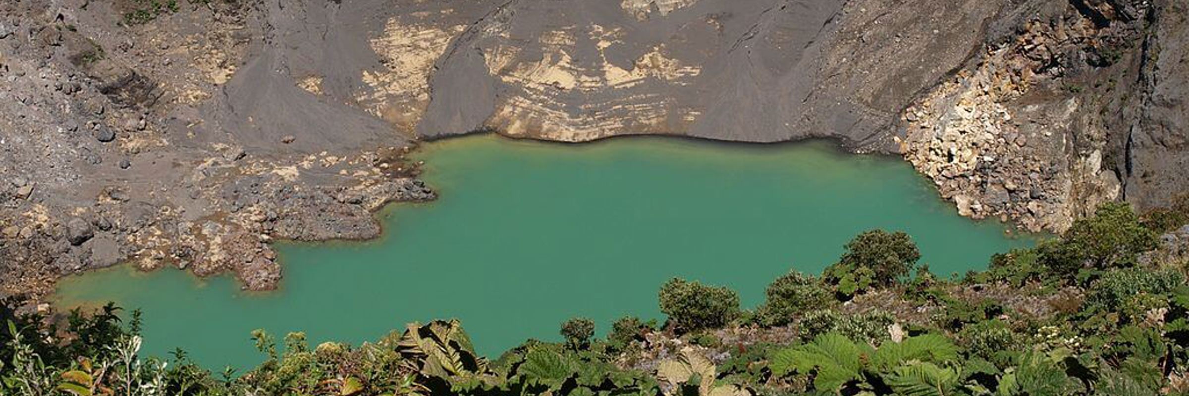 Emerald-green crater lake at Irazu Volcano, surrounded by rugged cliffs and alpine vegetation in Costa Rica. 