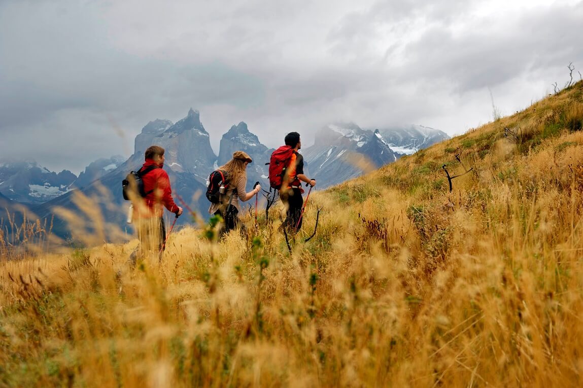 Group of trekkers hiking the W Trek in Torres del Paine with dramatic mountain peaks in the distance. 