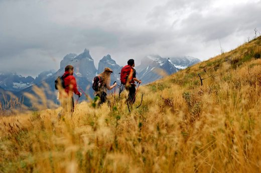 Group of trekkers hiking the W Trek in Torres del Paine with dramatic mountain peaks in the distance. 