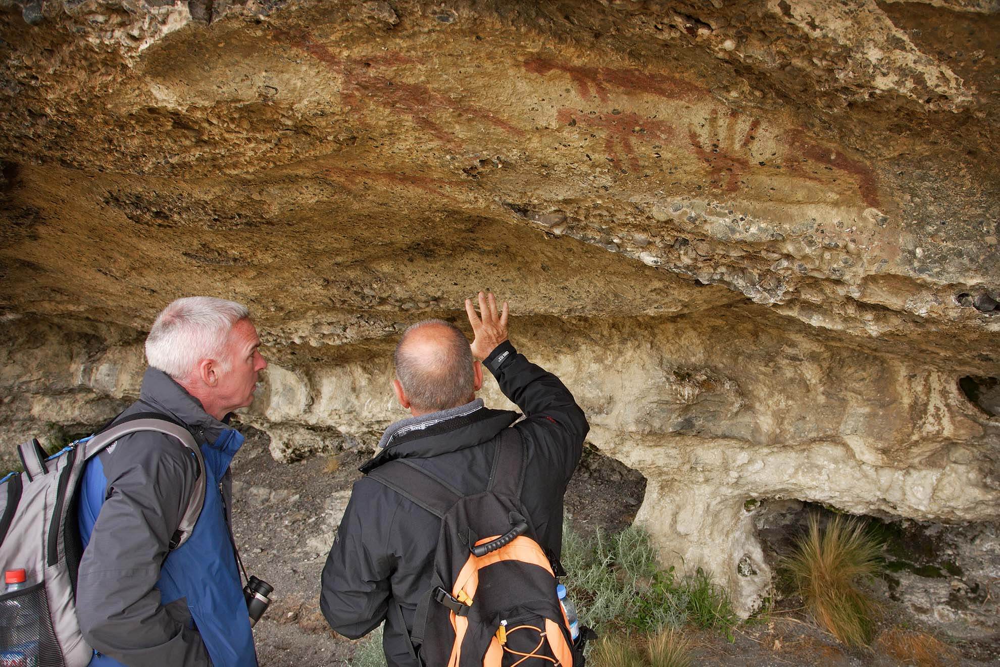 Two men examine ancient Aonikenk cave paintings in Patagonia on a cultural heritage hike near Torres del Paine, Chile. 