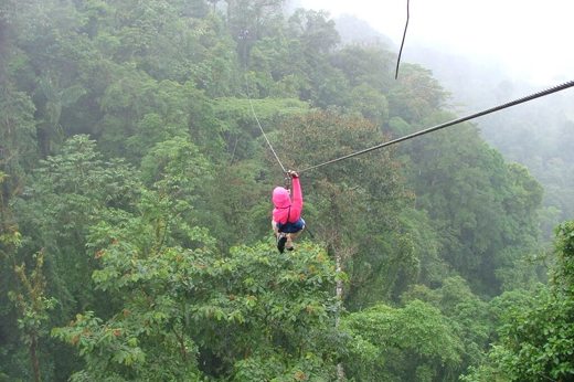 Adventurer ziplining high above the rainforest canopy in misty Costa Rican jungle. 