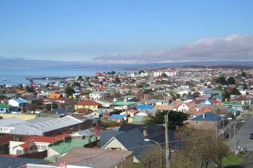 A panoramic view of colourful rooftops in Punta Arenas with the Straight of Magellan stretching out beneath a crisp blue sky. 