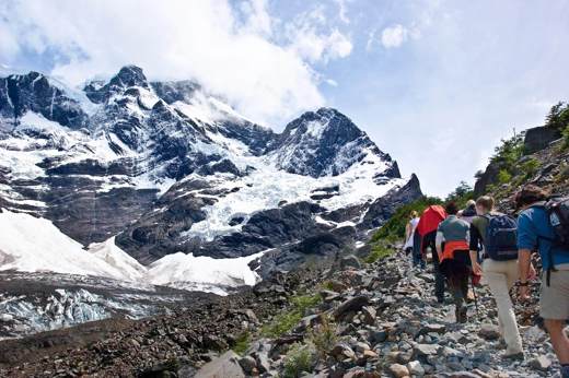 Group of hikers trekking through rocky trail in French Valley with snow-capped peaks and glaciers in Torres del Paine, Chile. 