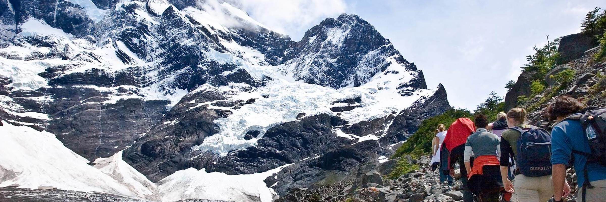 Group of hikers trekking through rocky trail in French Valley with snow-capped peaks and glaciers in Torres del Paine, Chile. 