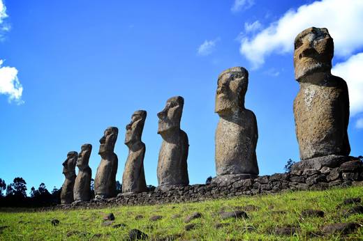 Row of seven restored moai statues at Ahu Akivi on Easter Island, set against a vivid blue sky and green grass. 