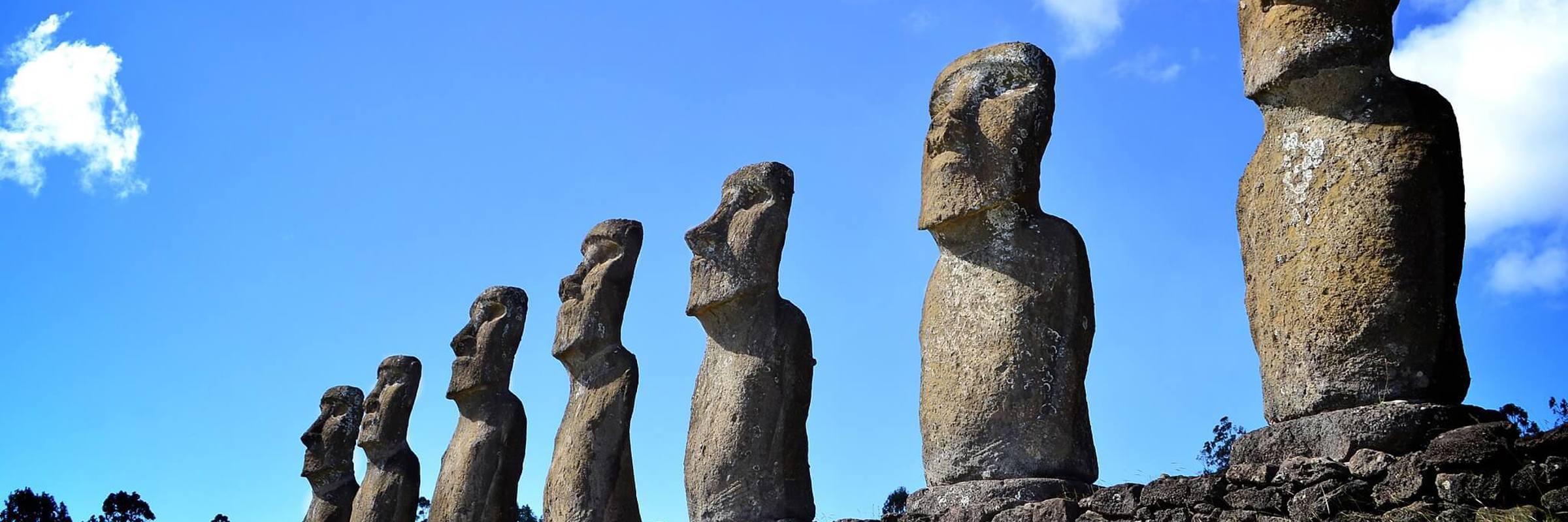 Row of seven restored moai statues at Ahu Akivi on Easter Island, set against a vivid blue sky and green grass. 