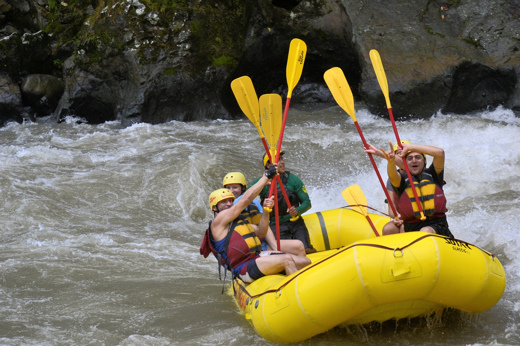 Adventurers paddle through white-water rapids on the Pacuare River in Costa Rica, all geared up in a bright yellow raft. 
