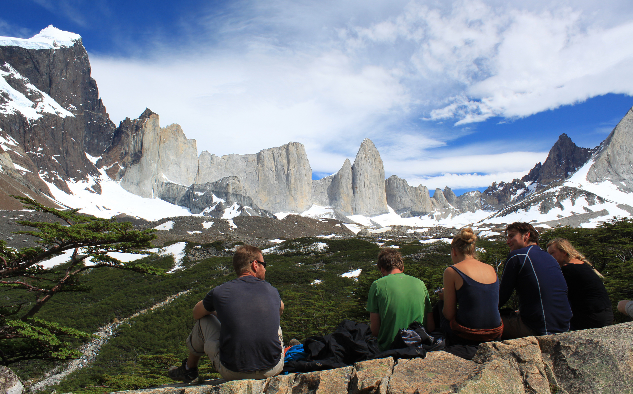 Hikers resting at a viewpoint overlooking the iconic granite spires of Torres del Paine in Chilean Patagonia. 