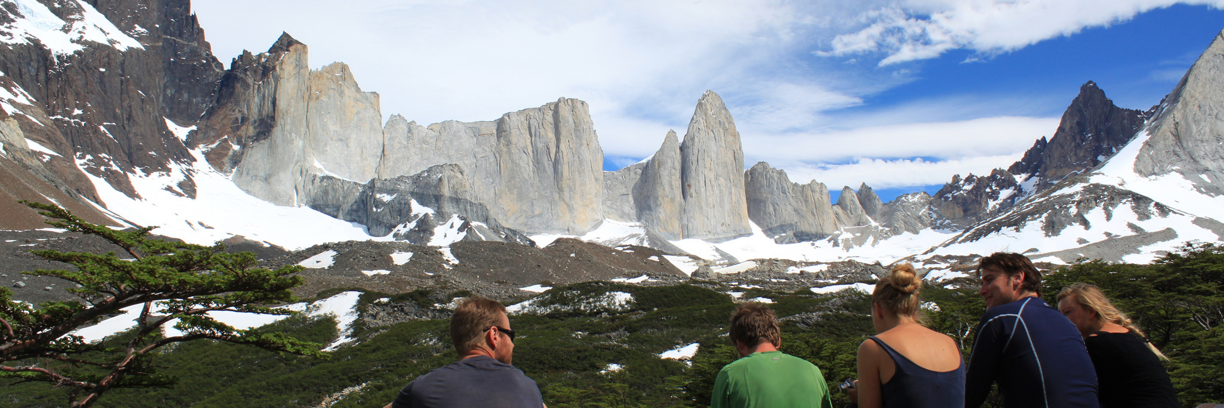 Hikers resting at a viewpoint overlooking the iconic granite spires of Torres del Paine in Chilean Patagonia. 