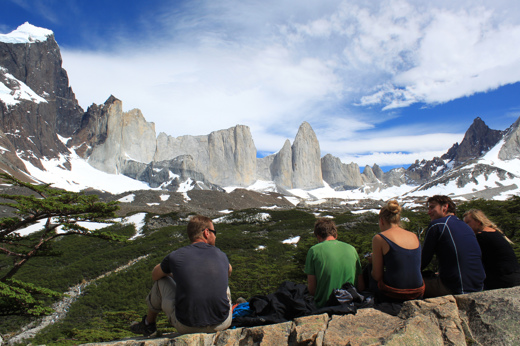 Hikers resting at a viewpoint overlooking the iconic granite spires of Torres del Paine in Chilean Patagonia. 