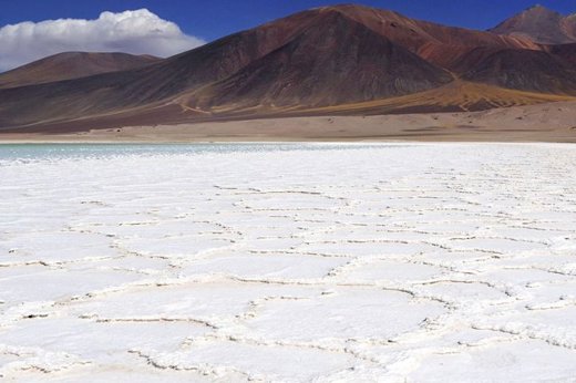 Vast salt flats stretch across the Atacama Desert, framed by distant mountains under a deep blue sky. 