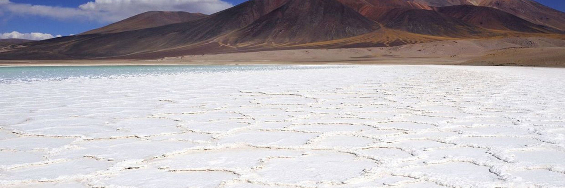 Vast salt flats stretch across the Atacama Desert, framed by distant mountains under a deep blue sky. 