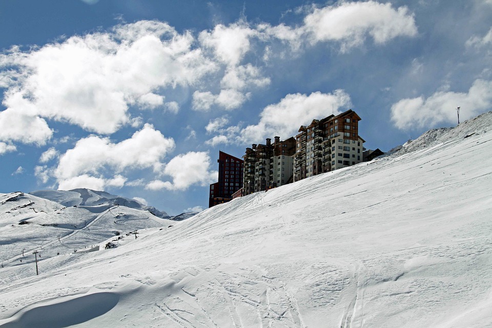 A ski resort building stands on a snowy slope beneath a sky dotted with fluffy clouds in Valle Nevado, Chile. 