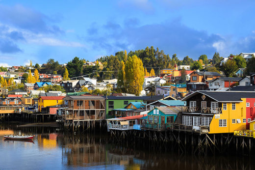 Colorful palafitos reflect in the calm waters of Castro, Chiloe Island, under a clear blue sky. 