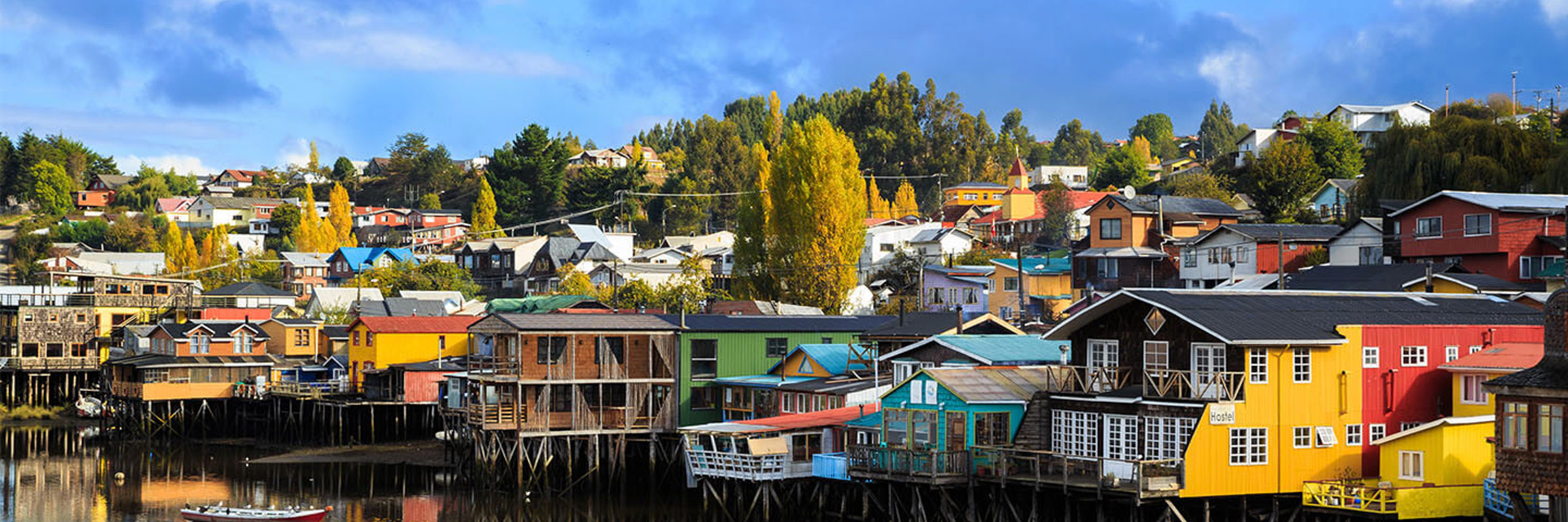 Colorful palafitos reflect in the calm waters of Castro, Chiloe Island, under a clear blue sky. 
