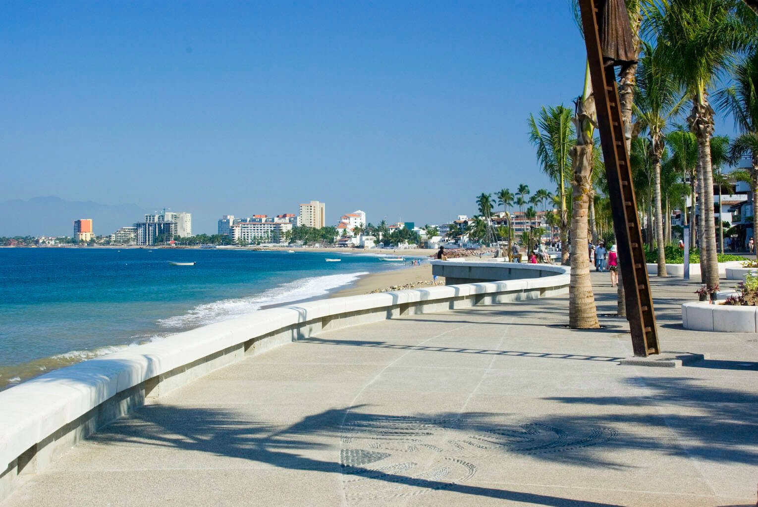 View of the Malecon promenade in Puerto Vallarta, Mexico, lined with palm trees, sculptures, and Pacific coastline views. 